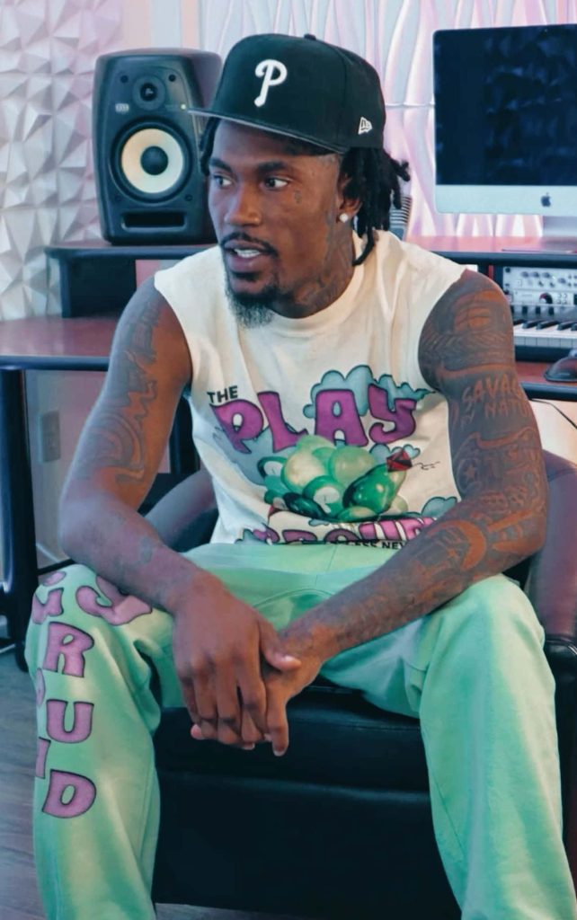 Rapper Hunxho in studio wearing graphic sleeveless tee and light green joggers with tattoos Wallpaper