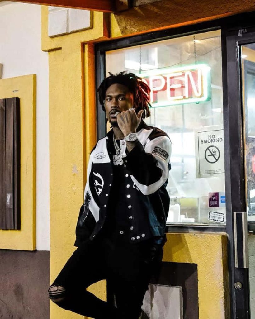 Hip hop rapper Hunxho in varsity jacket by vibrant yellow storefront with neon open sign wallpaper
