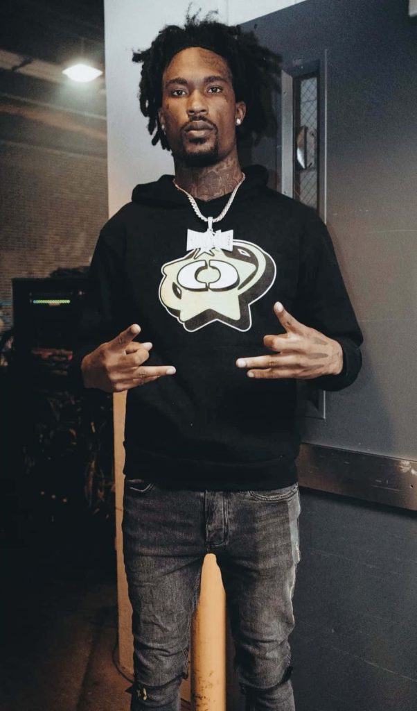 Portrait of rapper Hunxho in graphic hoodie silver chain with locs and facial tattoos in moody light Wallpaper