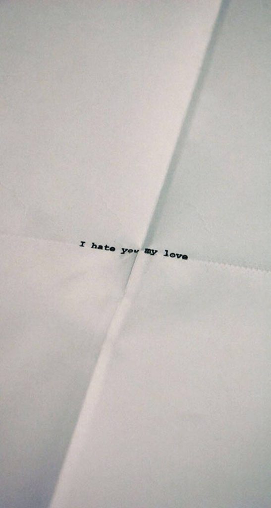 Minimalist wallpaper with phrase I hate you my love black ink on white paper with vertical crease