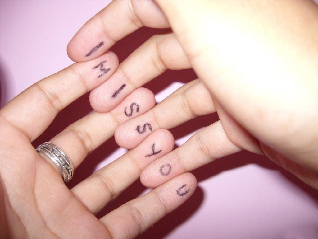 Close-up of fingers with ink letters spelling I Miss You silver ring pink background romantic wallpaper