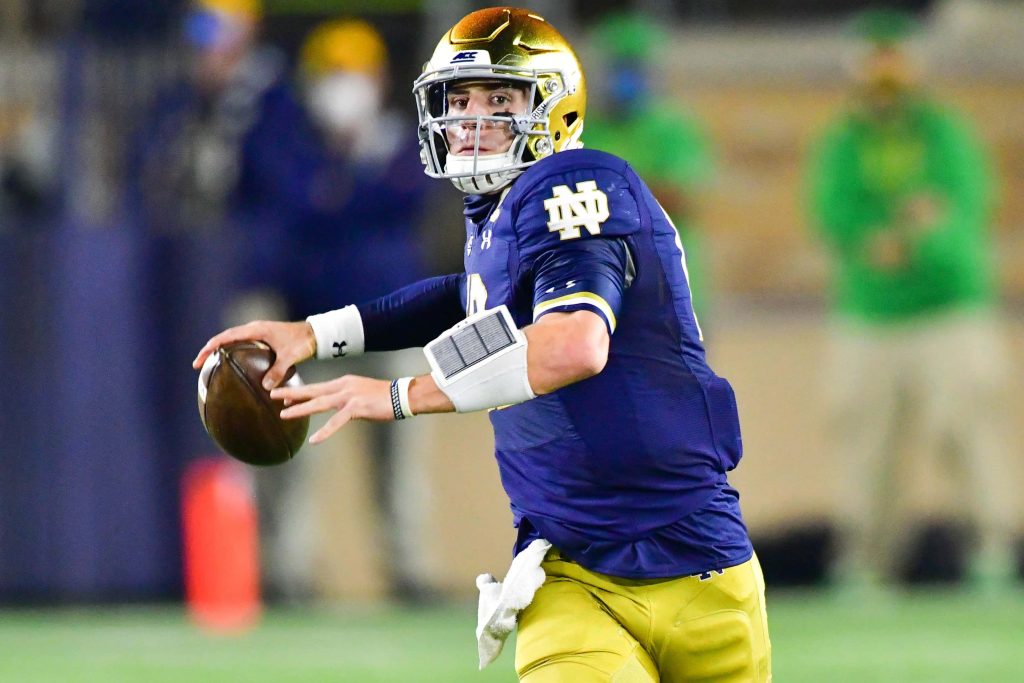 Notre Dame quarterback Ian Book in gold helmet navy uniform prepares to pass during game Wallpaper