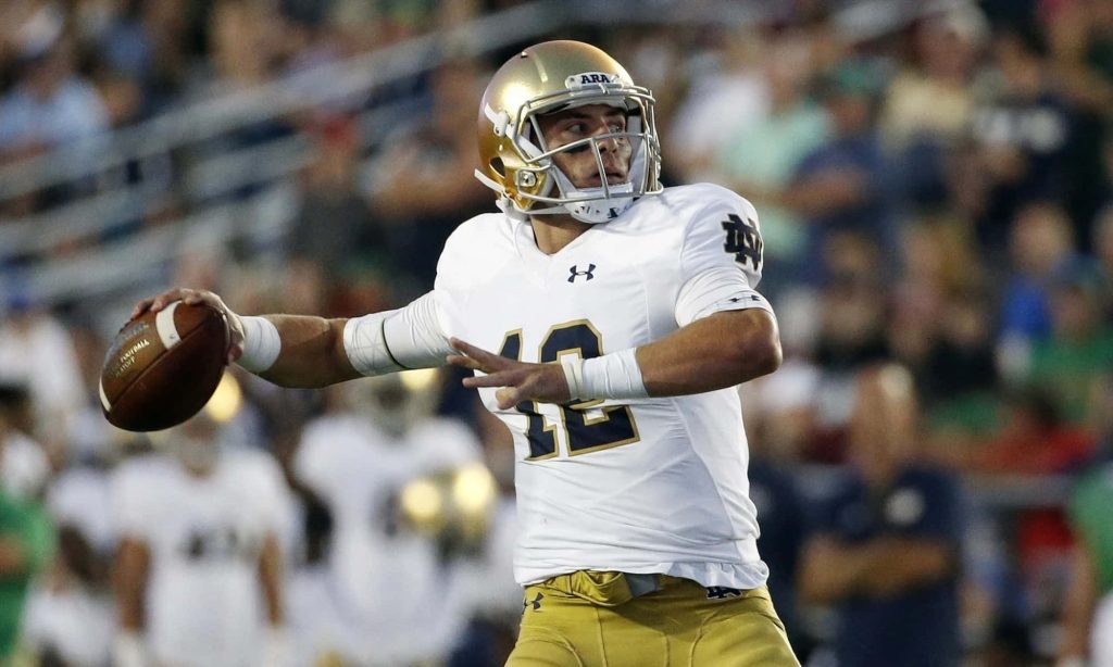 Ian Book Notre Dame quarterback in gold helmet and white jersey throwing a pass wallpaper