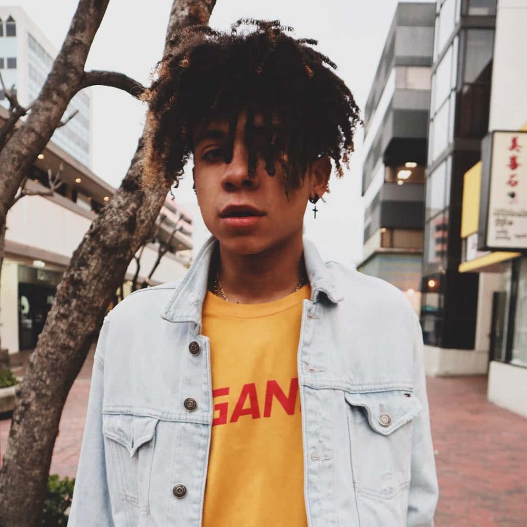 Iann Dior street portrait in light denim jacket yellow tee curly hair cross earring urban vibe wallpaper