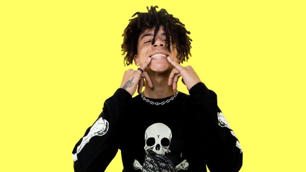 Vibrant Iann Dior portrait yellow background skull shirt silver chain hip-hop wallpaper