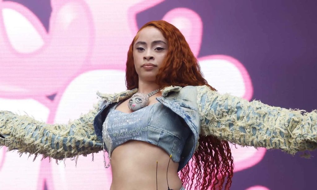 Ice Spice performing live with curly ginger hair in denim crop top pink background wallpaper