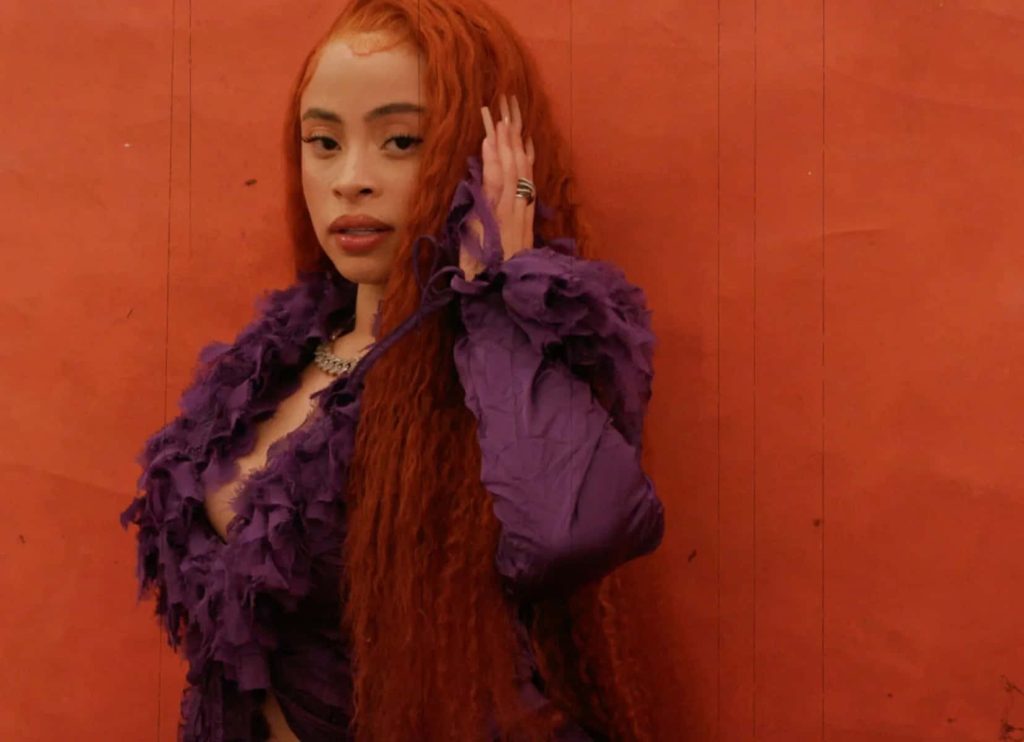 Ice Spice vibrant wallpaper rapper in purple ruffled top with long ginger curls on orange background