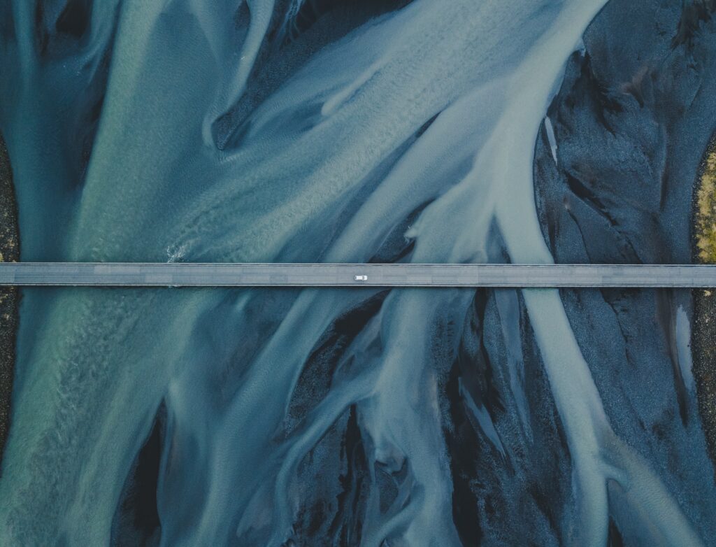 Aerial view of Iceland bridge over winding icy river with swirling blue and gray water patterns Wallpaper