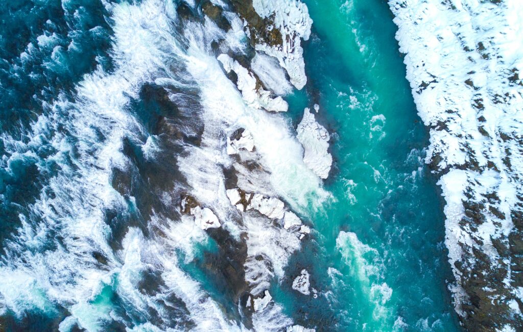 Aerial view of icy turquoise waters and rugged ice floes near a powerful Iceland waterfall winter landscape Wallpaper