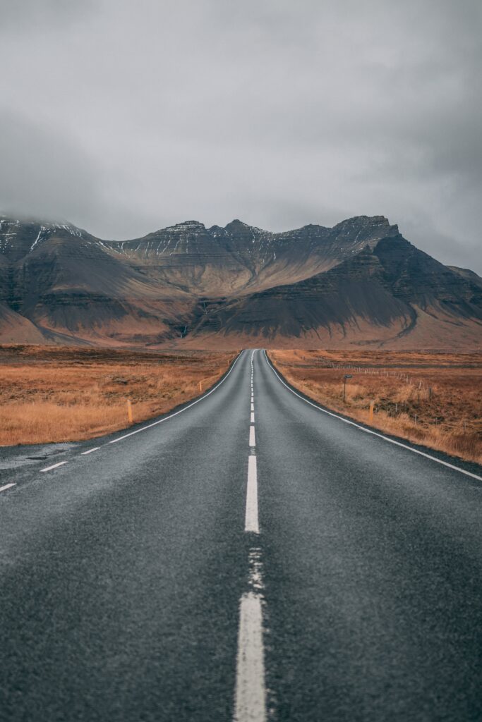 Straight Iceland road through rugged mountains and orange grass under cloudy sky landscape wallpaper