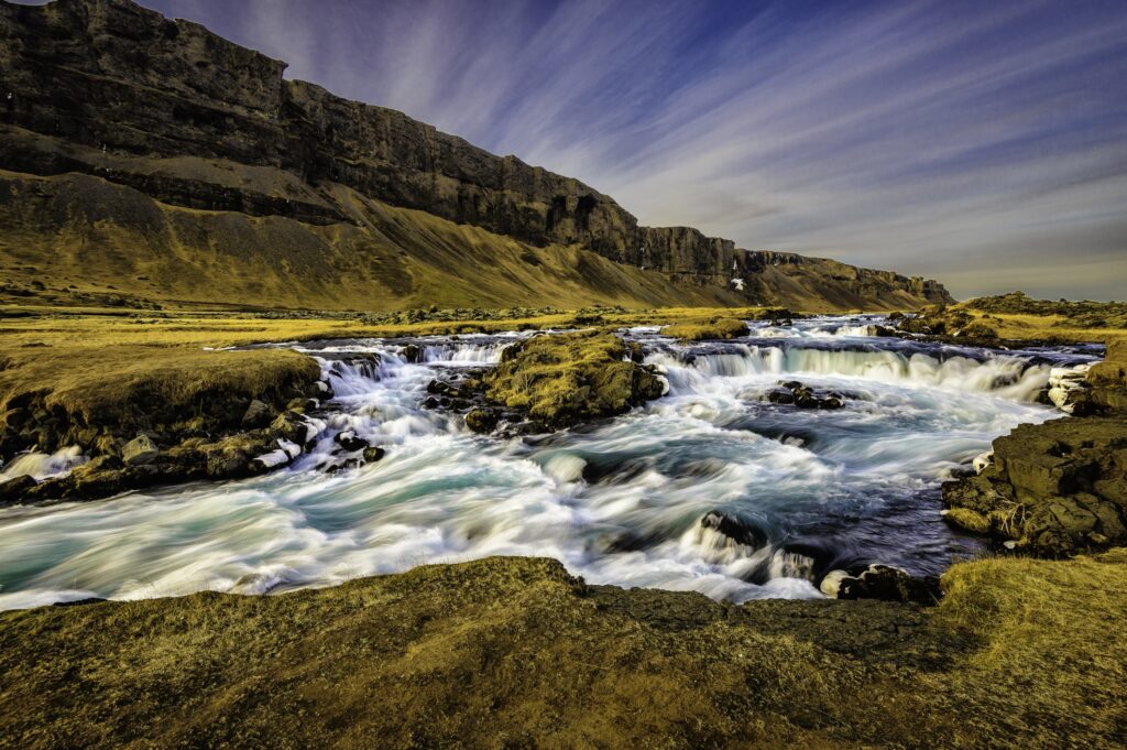 Icelandic landscape wallpaper with rushing river rugged rocks and vibrant blue gold sky background