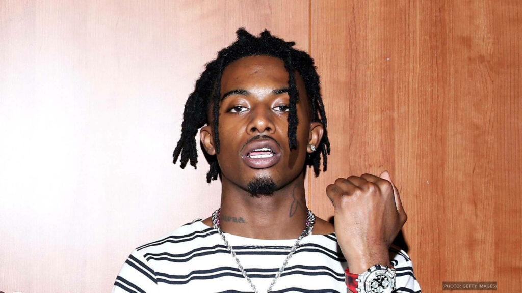 Stylish Playboi Carti with unique hairstyle posing in front of plain background Wallpaper