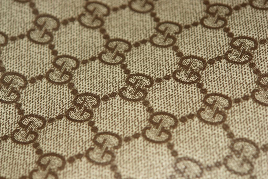Close-up Gucci brown GG monogram on textured beige canvas with soft lighting wallpaper background