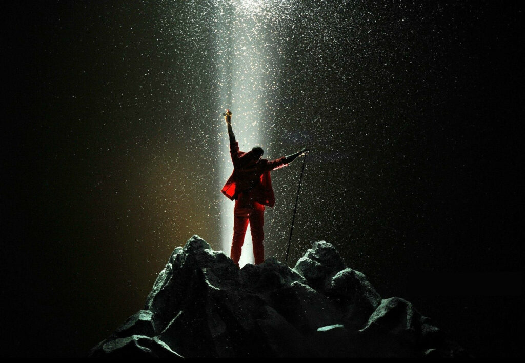 Iconic Kanye West Wallpaper: Triumph on Rocks with Dramatic Lights