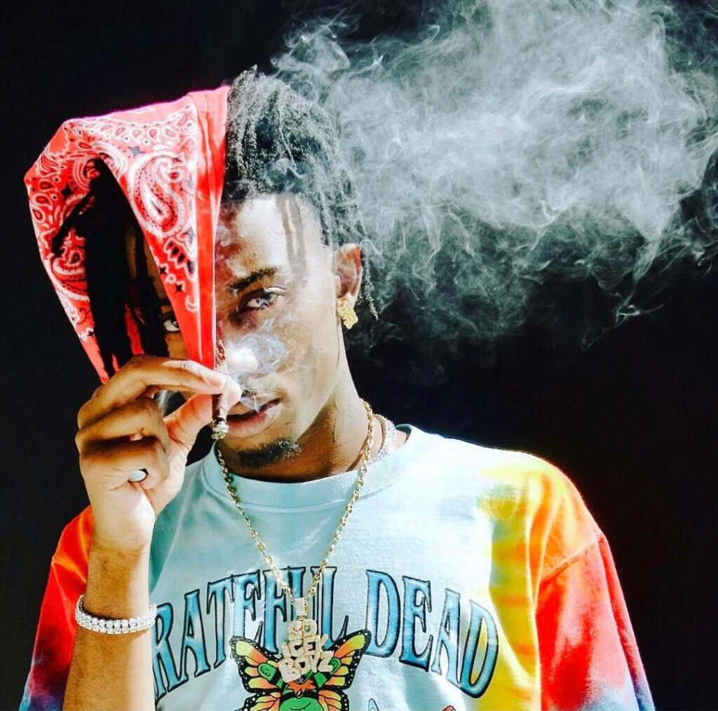 Edgy portrait of rapper Playboi Carti in red paisley bandana smoky scene with vintage Grateful Dead tee Wallpaper