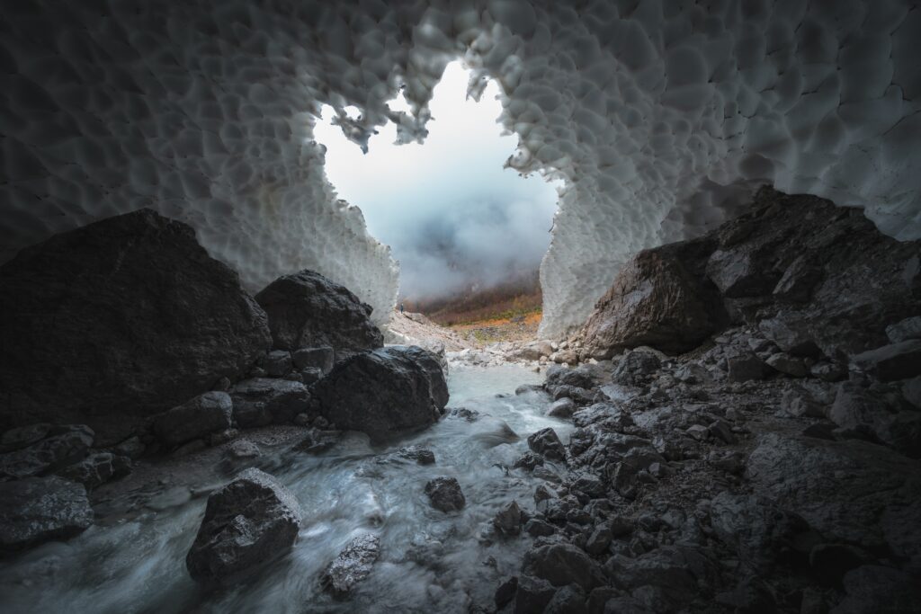 Icy cave interior with frozen formations and flowing stream revealing misty vibrant landscape outside Wallpaper