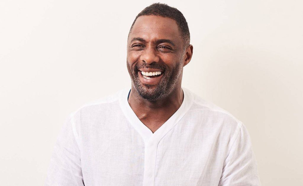 Idris Elba portrait smiling in white sweater bright studio background desktop wallpaper