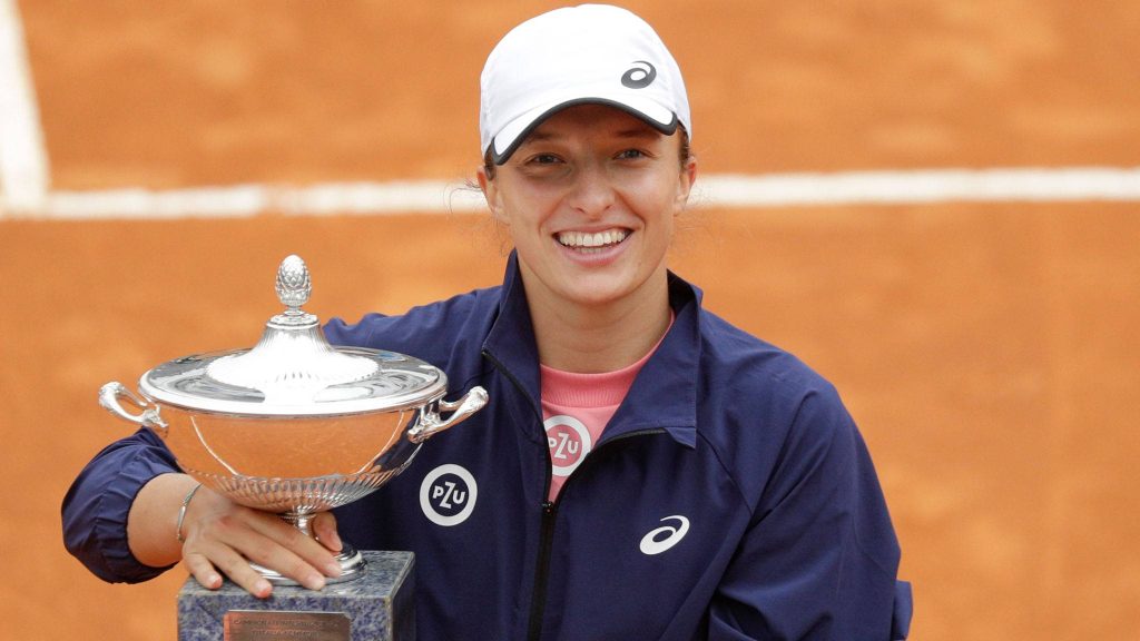 Iga Świątek smiling with silver Italian Open trophy on clay court wearing navy jacket and white cap Wallpaper