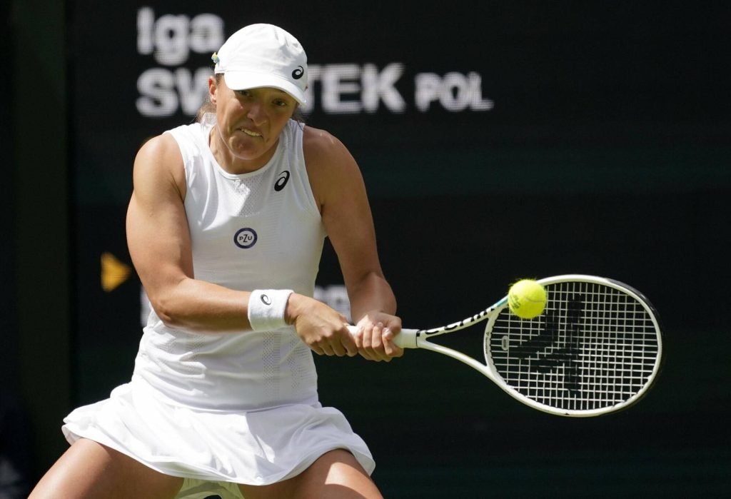 Iga Świątek powerful two-handed backhand tennis shot in white kit on dark stadium background Wallpaper