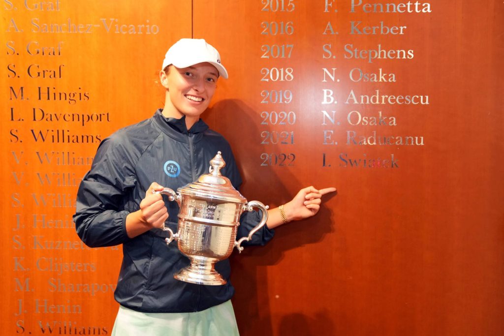 Tennis champion Iga Świątek celebrates 2022 US Open win holding silver trophy by champions wall Wallpaper
