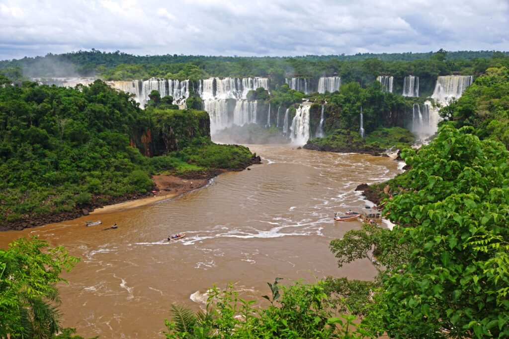 Iguazu waterfalls cascading into muddy river amid lush rainforest under cloudy sky wallpaper background