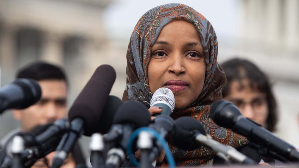 U.S. Representative Ilhan Omar addressing press conference wearing patterned hijab with microphones Wallpaper