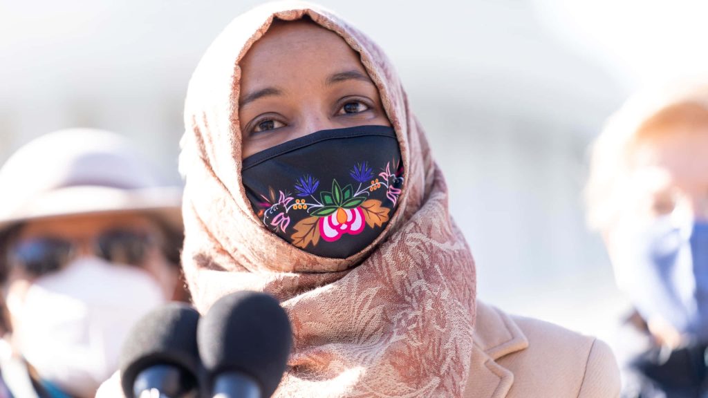 U.S. Representative Ilhan Omar speaking outdoors wearing patterned hijab and floral embroidered black mask Wallpaper