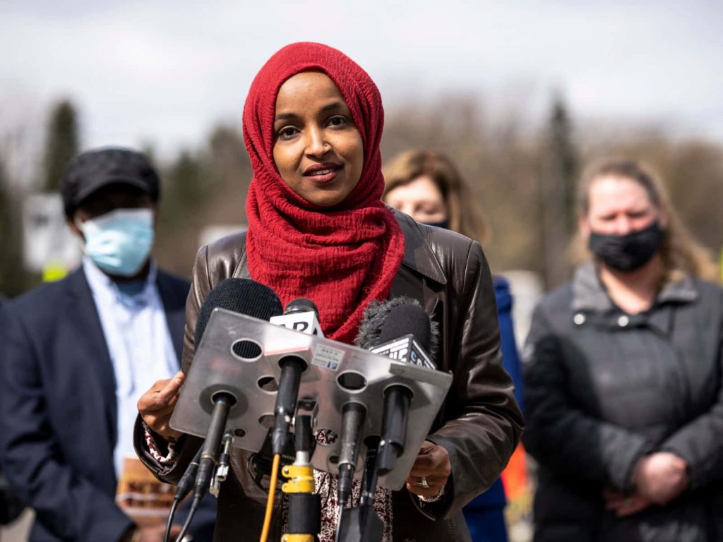 U.S. Representative Ilhan Omar speaking at outdoor press conference wearing red hijab and jacket Wallpaper