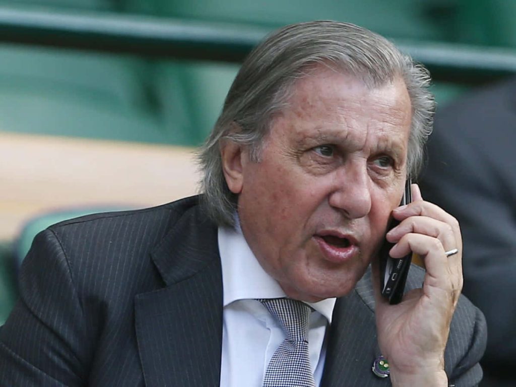 Ilie Năstase in formal suit on phone blurred green stadium background tennis legend wallpaper