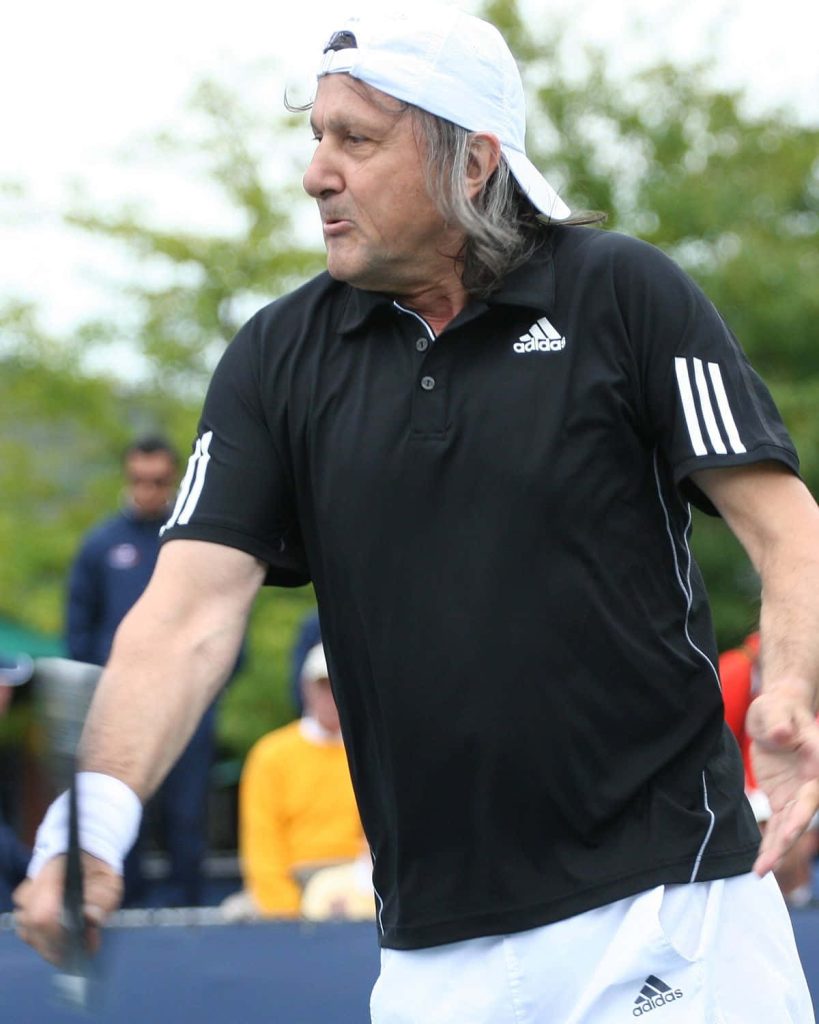 Ilie Năstase tennis icon mid-match wearing black Adidas polo and backwards cap on court Wallpaper