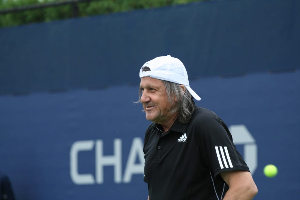 Ilie Năstase US Open tennis portrait in white cap and black Adidas shirt with flying ball Wallpaper