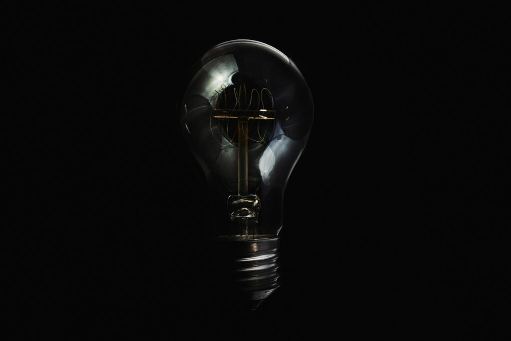 Luminous Vessel in Obscurity: Mesmerizing 4K Wallpaper featuring a Transparent Glass Light Bulb in Dark Ambience