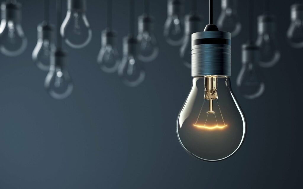 Glowing light bulb with warm filament on dark background symbolizing bright creative idea Wallpaper