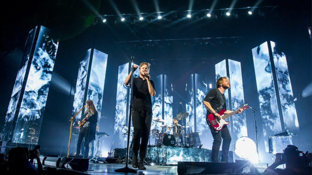 Imagine Dragons live World Tour concert with vibrant lights and dynamic stage visuals background Wallpaper