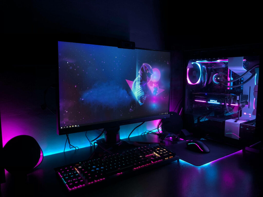 The Ultimate Gaming Oasis: Immersive Single Monitor Setup Illuminated by Mesmerizing Magenta and Cyan LED Backlights within a Dark Gaming Haven Wallpaper