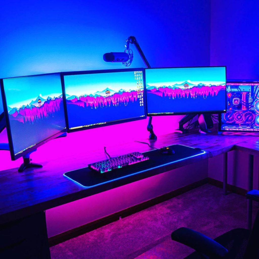 Immersive gaming room with triple monitors showing mountains and neon purple blue RGB lights Wallpaper