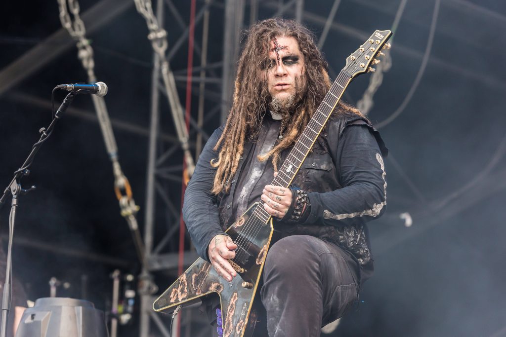 Metal guitarist with dreadlocks and haunting makeup plays distressed Schecter guitar live on stage Wallpaper