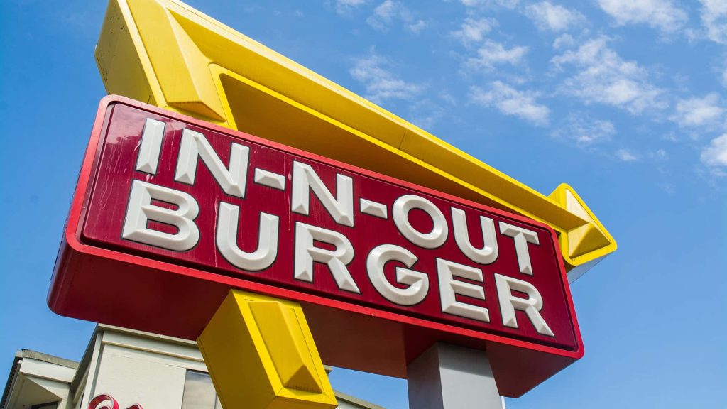 In-N-Out Burger pole sign with red white yellow branding against clear blue sky wallpaper background