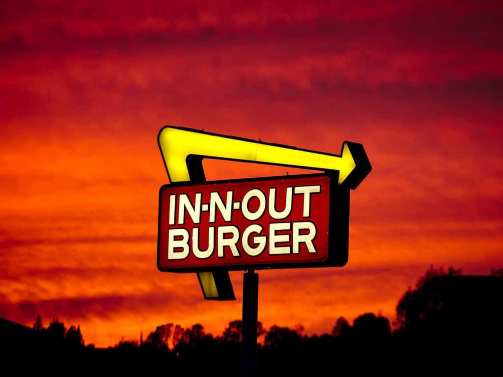 In-N-Out Burger sign glowing at sunset with vivid sky and silhouetted foliage wallpaper background
