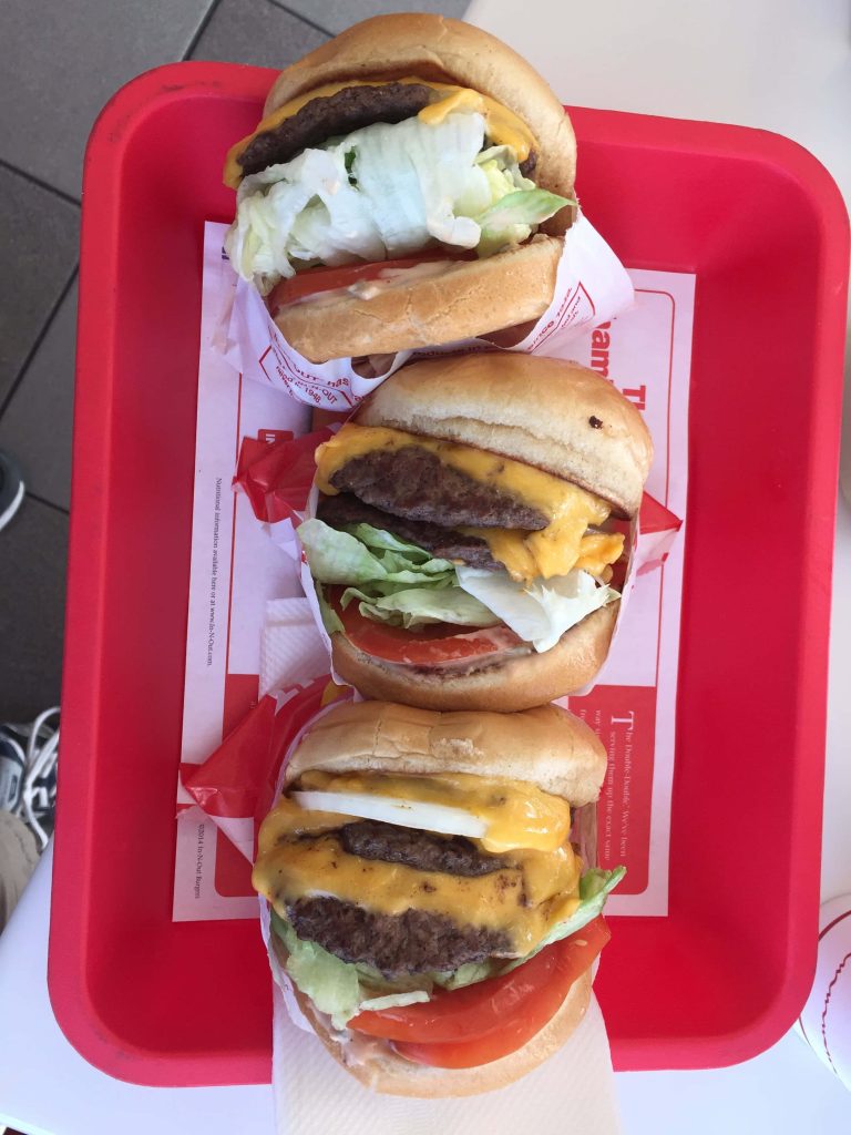 High-angle shot of three In-N-Out cheeseburgers on red tray with fresh lettuce tomato and melted cheese Wallpaper