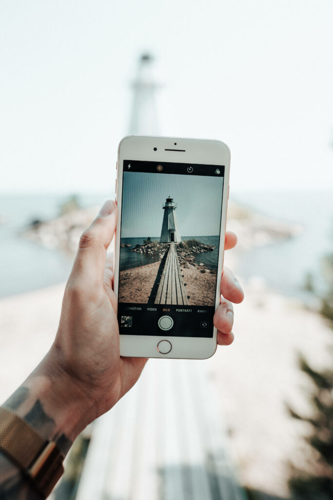 Capturing Serene Landscapes: A Photographer Using an iPhone to Frame a Majestic Lighthouse Wallpaper