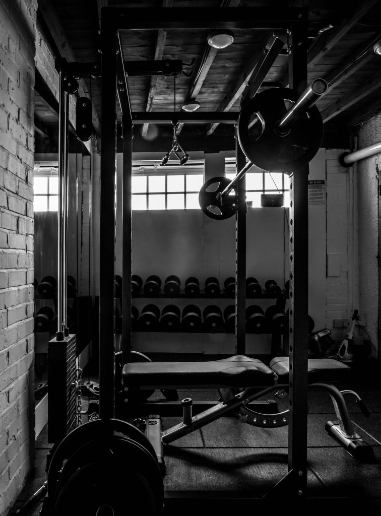 Black and white gym wallpaper with power rack dumbbells weight bench in industrial basement