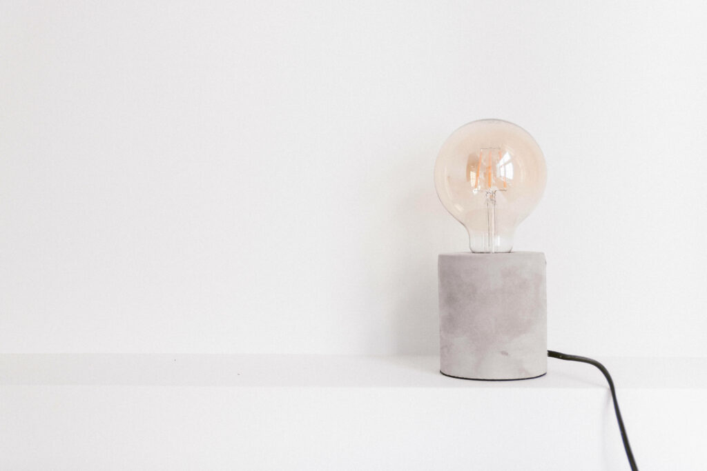 A Serene Composition Unveiling the Radiance of a Light Bulb Encased in a Subdued Gray Container on a Crisp White Table against a Pure White Backdrop Wallpaper