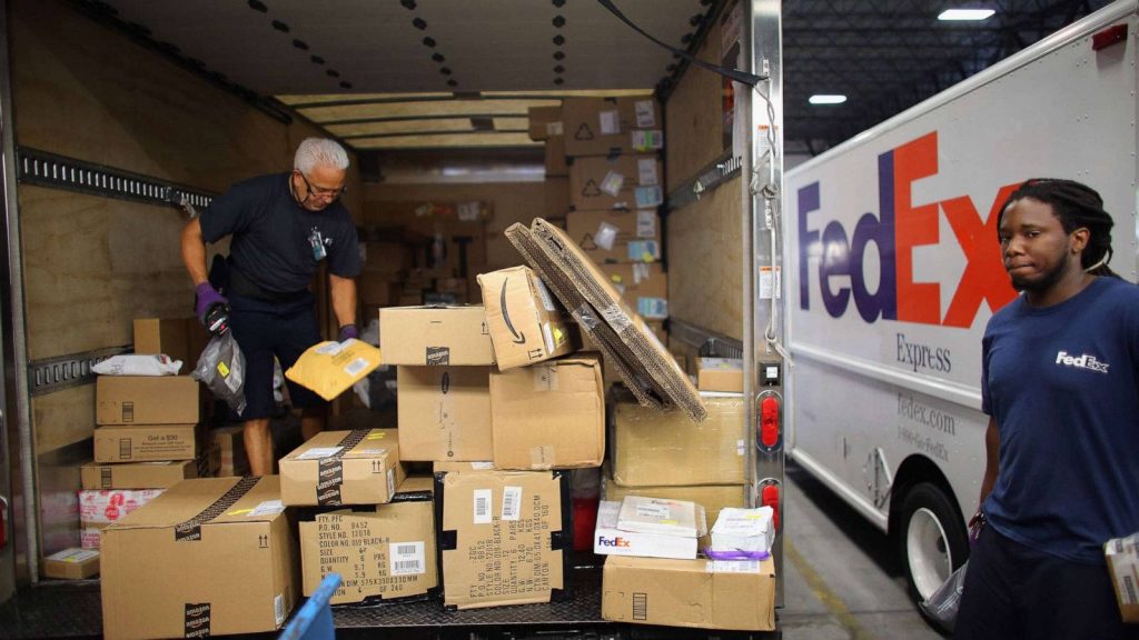 FedEx workers organizing Amazon packages in delivery truck scanning parcels for efficient logistics Wallpaper