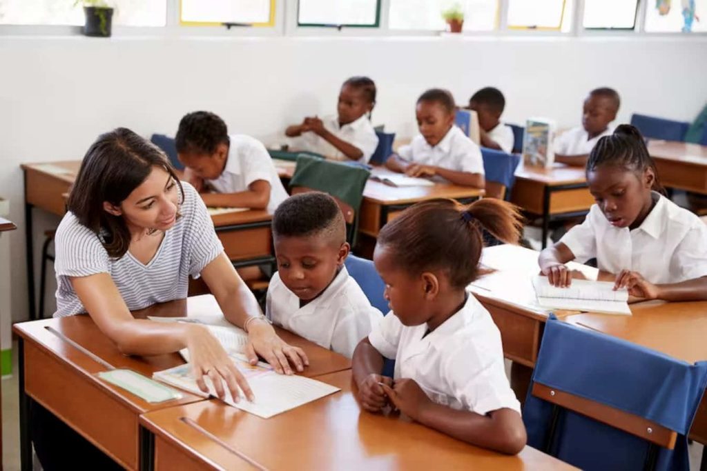 Dedicated teacher guiding focused students in bright classroom learning today leading tomorrow wallpaper