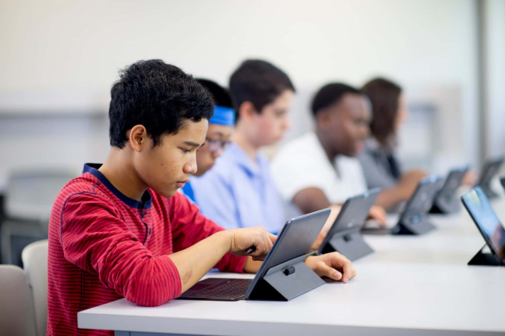 Diverse students using tablets in a bright classroom showing technology enhancing education Wallpaper