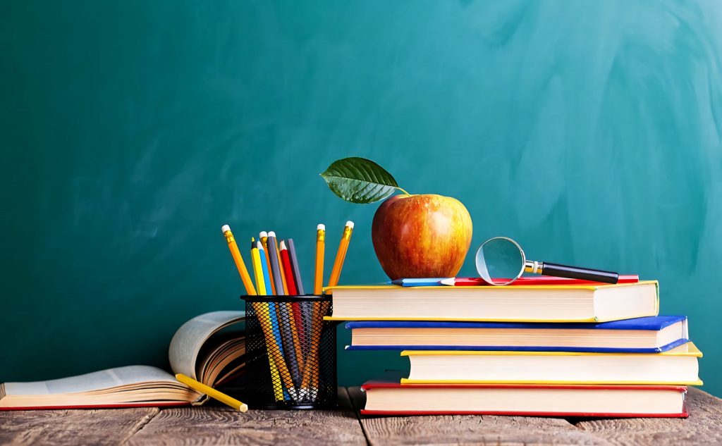 Colorful books red apple pencils on wooden desk green chalkboard education wallpaper background