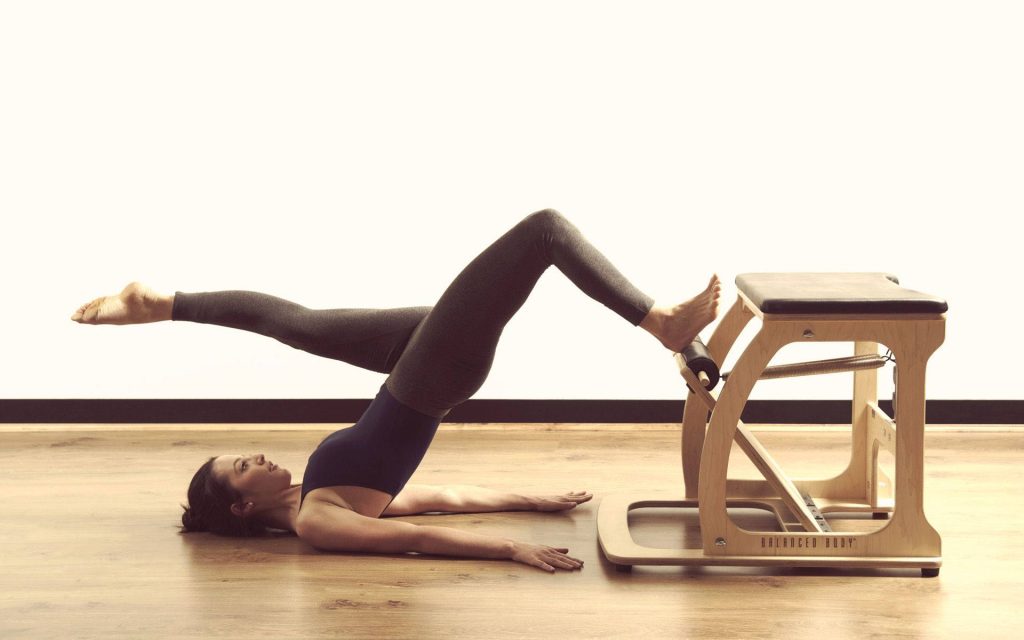 Woman practicing Pilates bridge pose on Balanced Body chair in bright minimalist studio wallpaper
