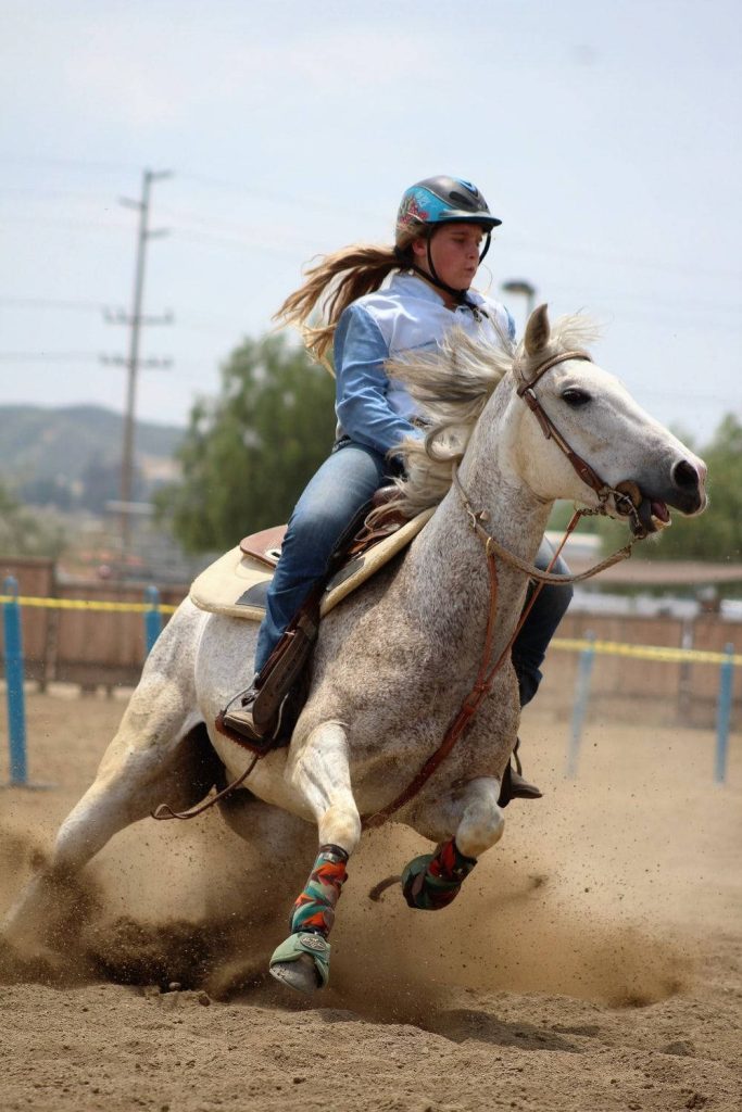 Rider and grey horse racing around barrel kicking up dust in intense barrel racing event Wallpaper