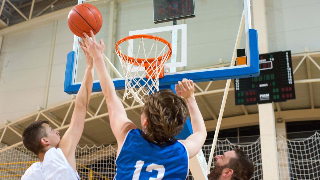 Two basketball players in blue and white jerseys leap for the ball near the hoop indoor gym Wallpaper